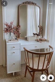 a white desk with a mirror, chair and flowers on it in front of a window