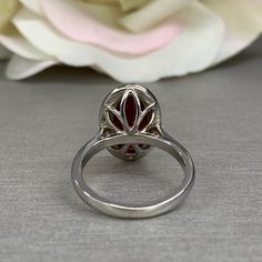 a close up of a ring with a flower in the middle and a white rose behind it