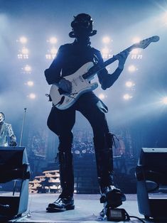 a man with a guitar standing on stage in front of an audience at a concert