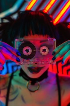 a woman holding up a cassette in front of her face with two eyeballs on it