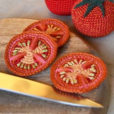 two crocheted tomatoes on a cutting board next to a knife and some fruit