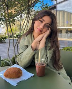 a woman sitting at a table with a drink and croissant in front of her