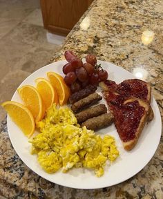 a white plate topped with breakfast foods on top of a marble countertop next to orange slices