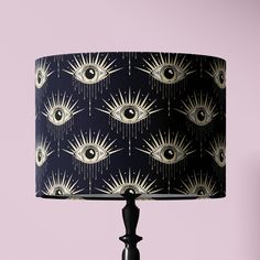 a black lamp with an all seeing eye shade on it's side and a pink wall behind it