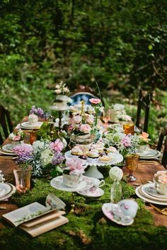 a table with plates, cups and saucers on it in the middle of a forest