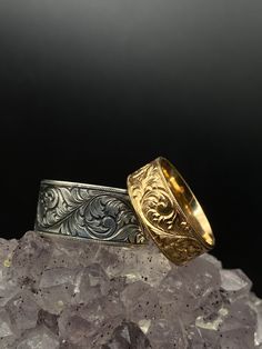 two gold and silver wedding bands sitting on top of some rock next to each other