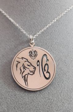 Are you looking for a special gift? How about this precious sterling silver pendant representing the Ik Onkar symbol, the Khanda sword, and the Lion? The Ik Onkar Symbol is the declaration of unity in Sikhism, that is 'there is only one God'. Ik Onkar are the first words of the Mul Mantar and also the opening words of the sacred Sikh scripture Guru Granth Sahib. The double-edged Khanda sword is a metaphor for Divine Knowledge, its sharp edges can separate truth from falsehood. Outside the circle Symbolic Medallion Jewelry For Commemoration, Symbolic Coin-shaped Jewelry With Large Pendant, Symbolic Jewelry With Large Coin Pendant, Symbolic Large Coin Pendant Jewelry, Symbolic Engraved Sterling Silver Necklaces, Symbolic Engraved Round Pendant Jewelry, Silver Medallion Necklace In Symbolic Style, Symbolic Medallion Necklace For Commemoration, Symbolic Engraved Jewelry For Commemoration