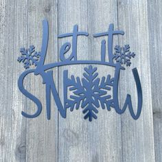 a metal sign that says let it snow on the side of a wooden fence with snowflakes