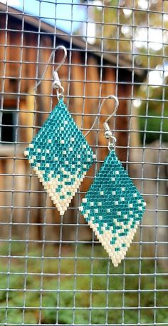 two square earrings hanging from a wire on a window sill in front of a house