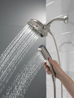 a person is holding the shower head in their hand and spraying it with water from the faucet