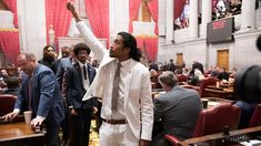 a man in white suit and tie standing in front of a room full of people