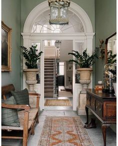 an entry way with green walls and white trim, wooden furniture and potted plants