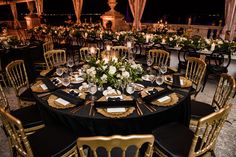 a table set up for an event with black linens and gold chairs