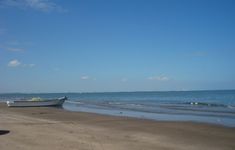 a boat sitting on top of a sandy beach next to the ocean's edge