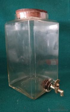 a clear glass container with a copper lid and spigot on the top, sitting on a green surface