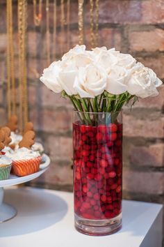 a vase filled with white flowers next to a plate of cupcakes on a table