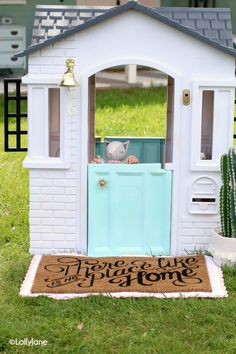 a toy house with a teddy bear in the door and welcome mat on the ground