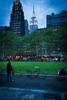 two people are standing in the middle of a park at night with skyscrapers in the background