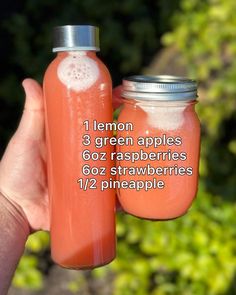 a hand holding a mason jar filled with orange liquid and labeled lemons, green apples, goz raspberries, 6oz strawberries, 1 / 2 / 2 / 2 / 2 pineapple