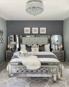 a bedroom with gray walls and white bedding, chandelier above the bed