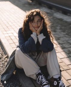 a woman sitting on the ground with her hands to her face and looking at the camera