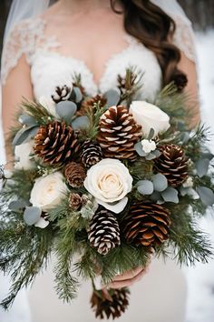 a bride holding a bouquet with pine cones and flowers