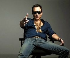 a man sitting in a chair wearing sunglasses and pointing to the side with his finger