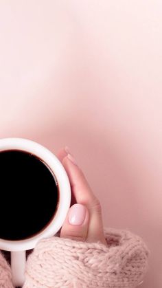 a woman holding a cup of coffee in her hands while wearing pink sweater and mittens