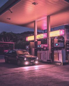 a car is parked in front of a gas station at night with its lights on