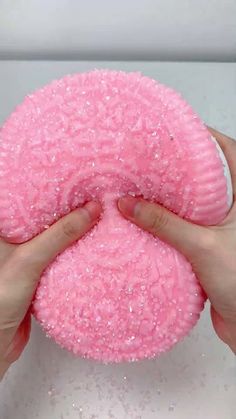 a person holding a pink doughnut with sprinkles on it in their hands