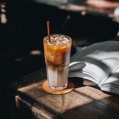 an iced latte sits on a table next to an open book with a straw in it