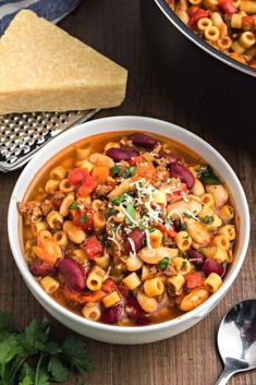 two bowls filled with pasta and vegetables on top of a wooden table next to silver spoons