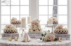 a table topped with lots of cakes covered in frosting next to candles and flowers