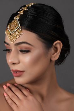 a woman wearing a gold headpiece with jewels on her forehead and hands around her neck