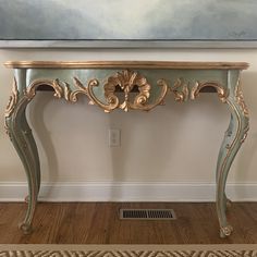 an antique console table painted in blue and gold with flowers on the top, against a white wall