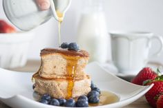 someone pouring syrup on some pancakes with blueberries and strawberries