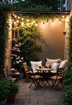 an outdoor dining area with lights strung over the table and chairs, surrounded by greenery