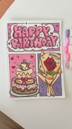 a happy birthday card with candles on the table next to it and some pens in front of it