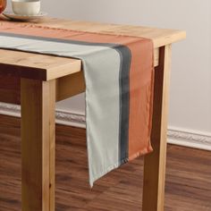 an orange and grey striped table runner on a wooden table with a bowl of fruit