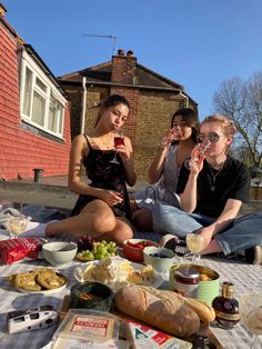 three women sitting on a blanket eating food and drinking wine together, with the woman holding a glass of wine in her hand