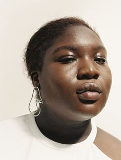 a woman with large hoop earrings on her face looking off to the side while wearing a white shirt