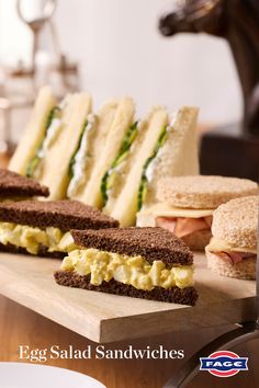 an egg salad sandwich is displayed on a cutting board with other sandwiches in the background