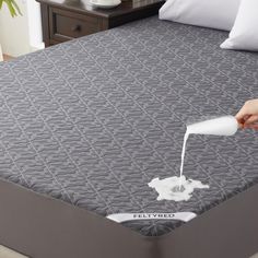 someone is pouring milk on a mattress in a room with white pillows and gray bedding