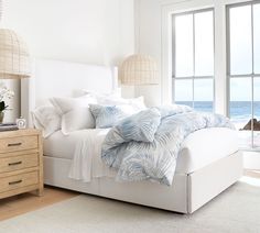 a bedroom with a bed, dresser and large window overlooking the ocean in front of it