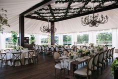 a dining room set up with white linens and greenery on the ceiling, along with chandeliers