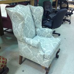 an upholstered chair in a room with other chairs and desks behind it