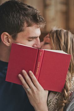 a man kissing a woman while holding a red book over his face in front of her