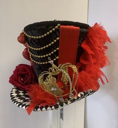 a black hat with red and gold decorations on it's side, next to a rose