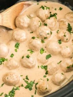 a wooden spoon is in a slow cooker filled with meatballs and gravy