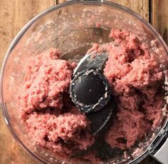 a food processor filled with pink stuff on top of a wooden table next to a blender